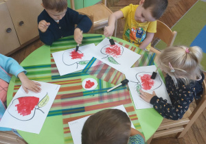 Dzieci siedzą przy stoliku i kolorują obrazek przedstawiający jabłko