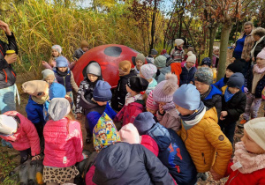 Dzieci stoją przy bardzo dużej figurze owada, pan przewodnik opowiada o nim dzieciom