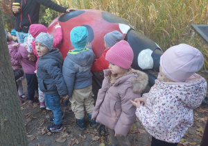 Dzieci stoją przy bardzo dużej figurze owada, pan przewodnik opowiada o nim dzieciom