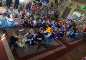 Dzieci siedzą na dywanie tworząc trzy rzędy. Dzieci siedzą jedno za drugim.jpeg