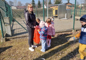 Pani trzyma worek na śmieci. Dzieci wrzucają do niego zebrane śmieci