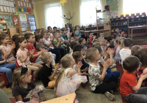 Dzieci siedzą na dywanie i klaszczą
