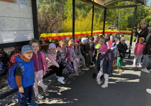Dzieci siedzą na przystanku autobusowym. Czekają na autobus