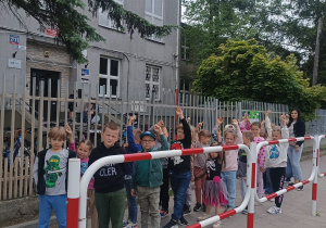 Dzieci stoją w parach pod szkołą, machają