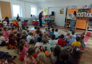 Dzieci siedzą na dywanie, zespół muzyczny gra na instrumentach