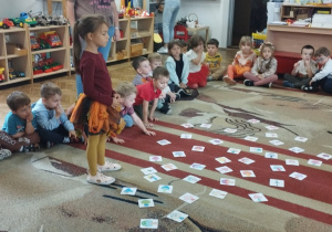 Dzieci siedzą na dywanie. Dziewczynka układa obrazki