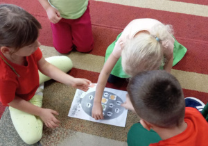 Dzieci siedzą na dywanie, rozwiązują łamigłówkę