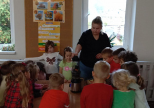 Dzieci patrzą jak nauczyciel wrzuca jabłka do wyciskarki