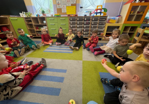 Dzieci siedzą na dywanie i trzymają jabłko