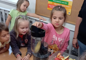 Dziewczynka wkłada jabłko do wyciskarki