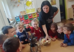 Dzieci patrzą jak pani wrzuca jabłka do wyciskarki