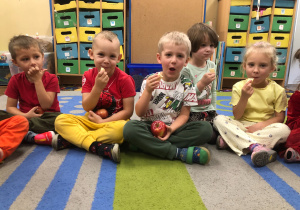 Dzieci siedzą na dywanie i jedzą jabłko