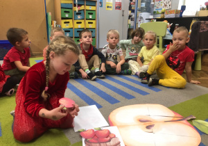 Dzieci siedzą na dywanie. Dziewczynka układa jabłka