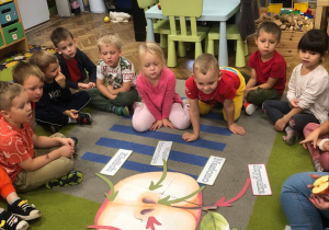 Dzieci siedzą na dywanie. Oglądają rozłożony plakat z budową jabłka