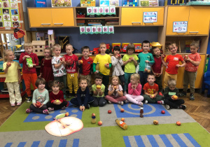 Dzieci pozują do zdjęcia grupowego, każde trzyma w dłoni jabłko