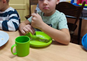 Chłopiec siedzi przy stole, trzyma widelec