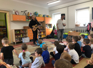 Pan gra na gitarze, drugi pan śpiewa. Dzieci siedzą na dywanie