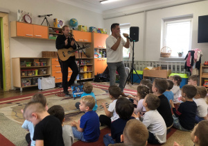 Pan gra na gitarze, drugi pan śpiewa. Dzieci siedzą na dywanie