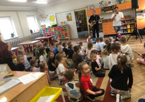 Pan gra na gitarze, drugi pan śpiewa. Dzieci siedzą na dywanie