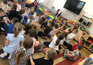 Dzieci siedzą na dywanie, klaszczą