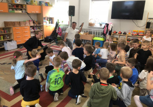 Pan gra na gitarze, drugi pan śpiewa. Dzieci siedzą na dywanie