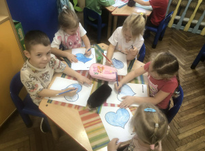 Dzieci siedzą przy stole, kolorują serca