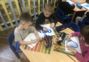 Dzieci siedzą przy stole, kolorują serca