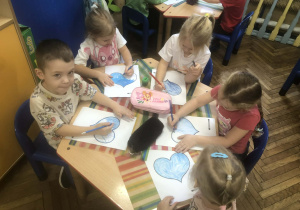 Dzieci siedzą przy stole, kolorują serca