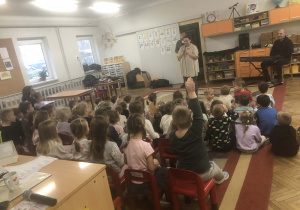 Dzieci siedzą na dywanie. Zespół występuje