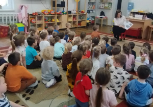 Dzieci siedzą na dywanie. Pani czyta opowiadanie.