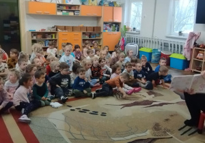 Dzieci siedzą na dywanie. Pani czyta opowiadanie.