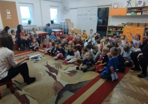 Dzieci siedzą na dywanie. Pani czyta opowiadanie.