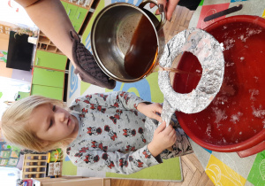 Dziewczynka trzyma klucz nad miską z wodą, przez który pani przelewa wosk