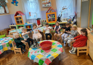 Dzieci siedzą na krzesłach wokół stolika, na którym stoi miska z wodą