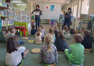 Dzieci siedzą na dywanie i słuchają jak Pani z biblioteki opowiada o Japonii